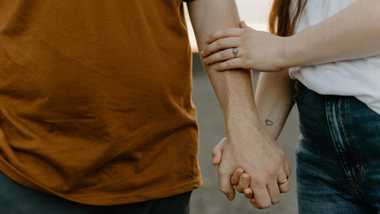 Close-up of two people holding hands while one rests their other hand on an arm.