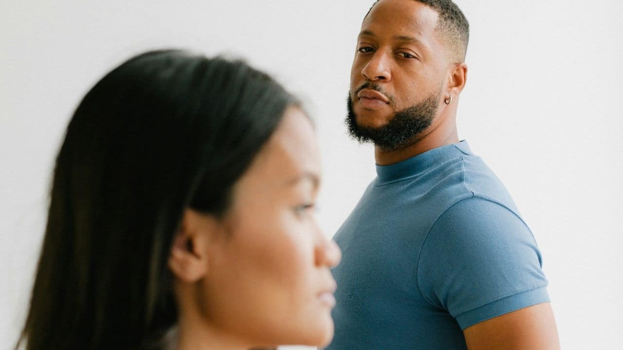 A man with a serious expression looks toward a woman who is facing away.
