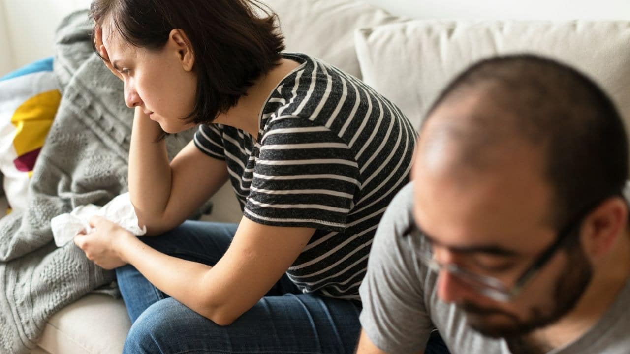 A woman in a striped shirt sits on a sofa looking away from a man.