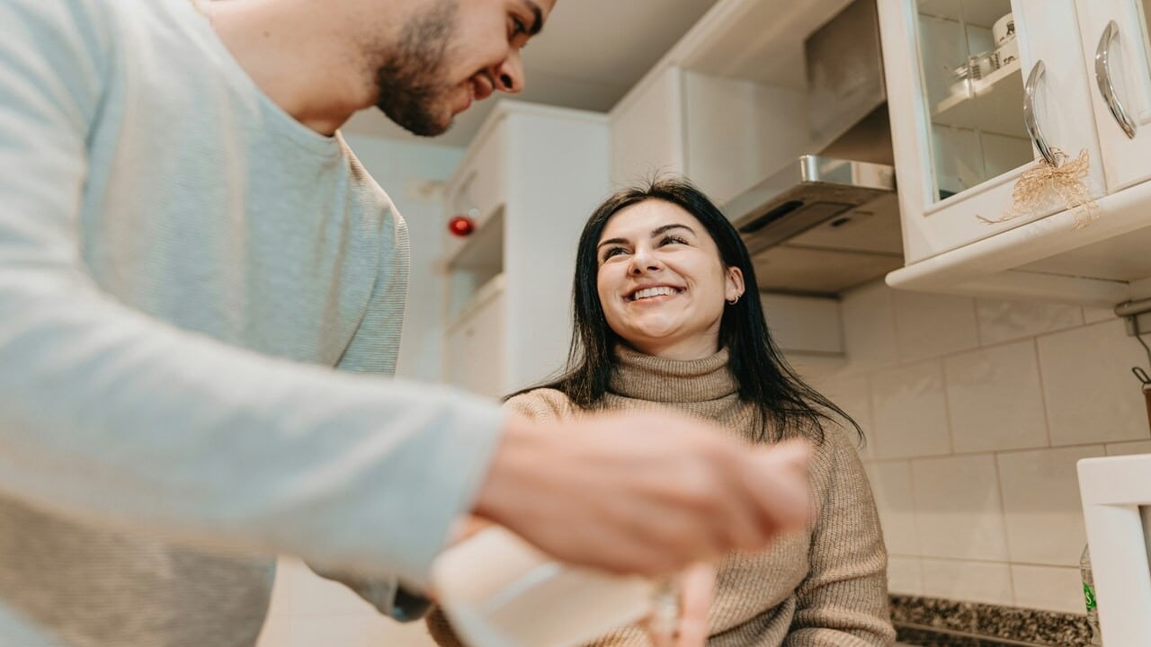 A couple smiling at each other in the kitchen