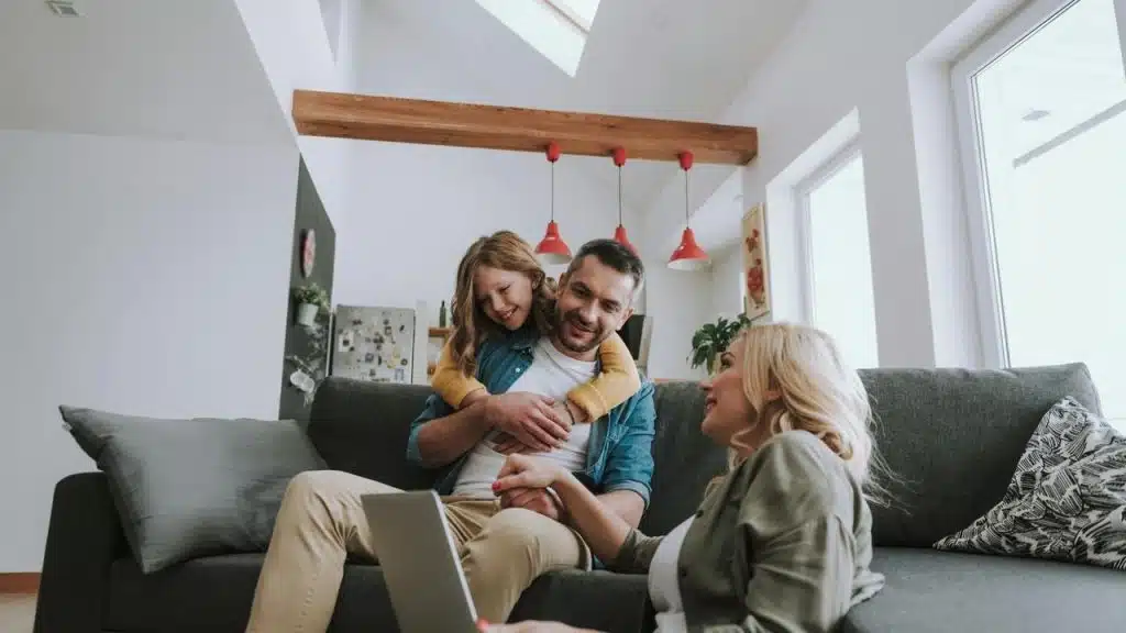 A family relaxes on a couch while a child hugs their father.