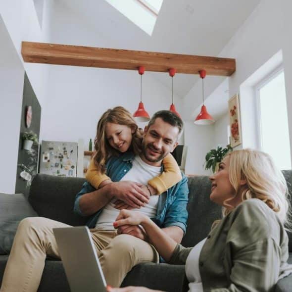 A family relaxes on a couch while a child hugs their father.