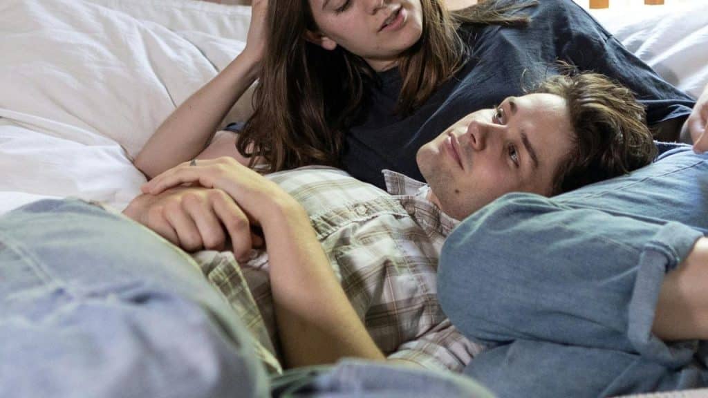 A couple lying on a bed holding hands.