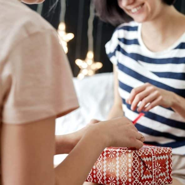 A smiling woman receives a wrapped gift box from another person.