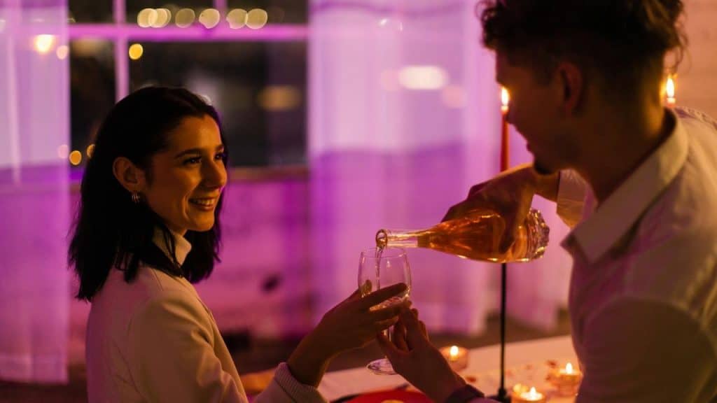 A couple shares a romantic candlelit dinner as one person pours wine into a glass.