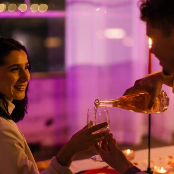 A couple shares a romantic candlelit dinner as one person pours wine into a glass.