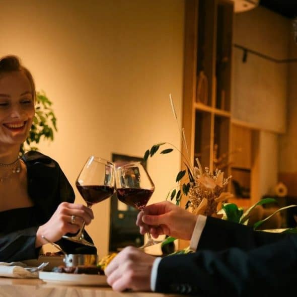 A couple in formal attire clinking glasses of red wine at a cozy restaurant table.