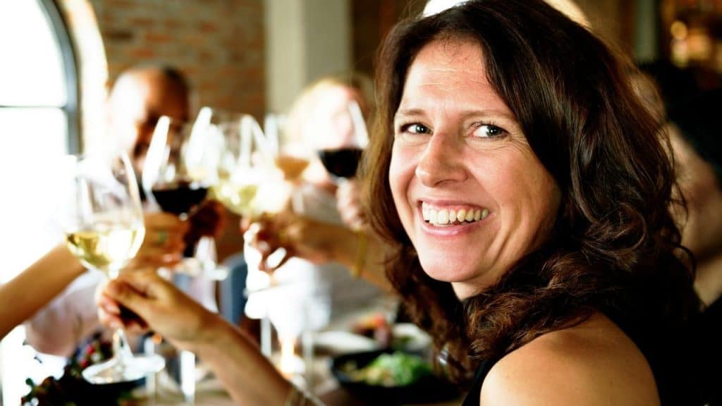 A smiling woman holding a glass of wine at a lively restaurant gathering.