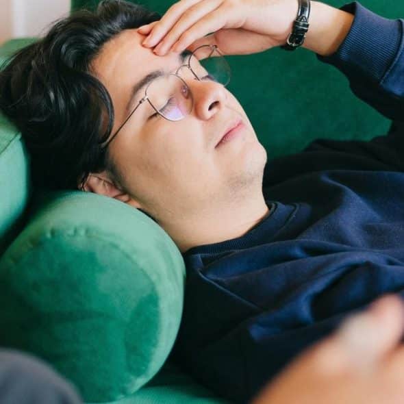 A man lies on a green couch with his hand on his forehead.