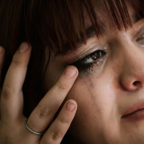 A close-up of a woman with tears and smudged makeup.