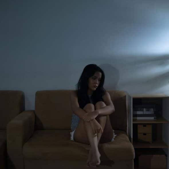 A woman sits alone on a couch in a dimly lit room.