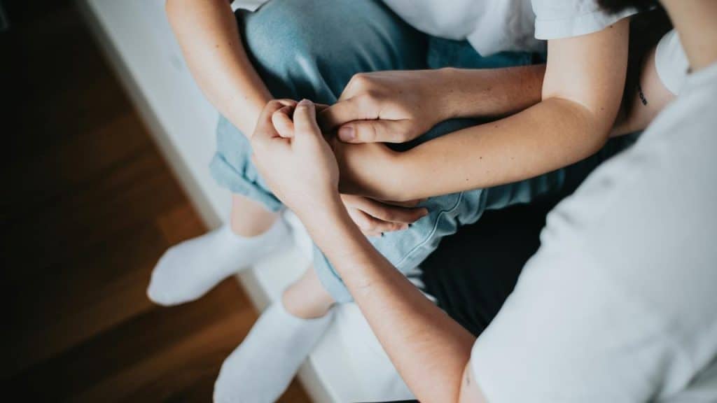 A person holds another’s hand in comfort.