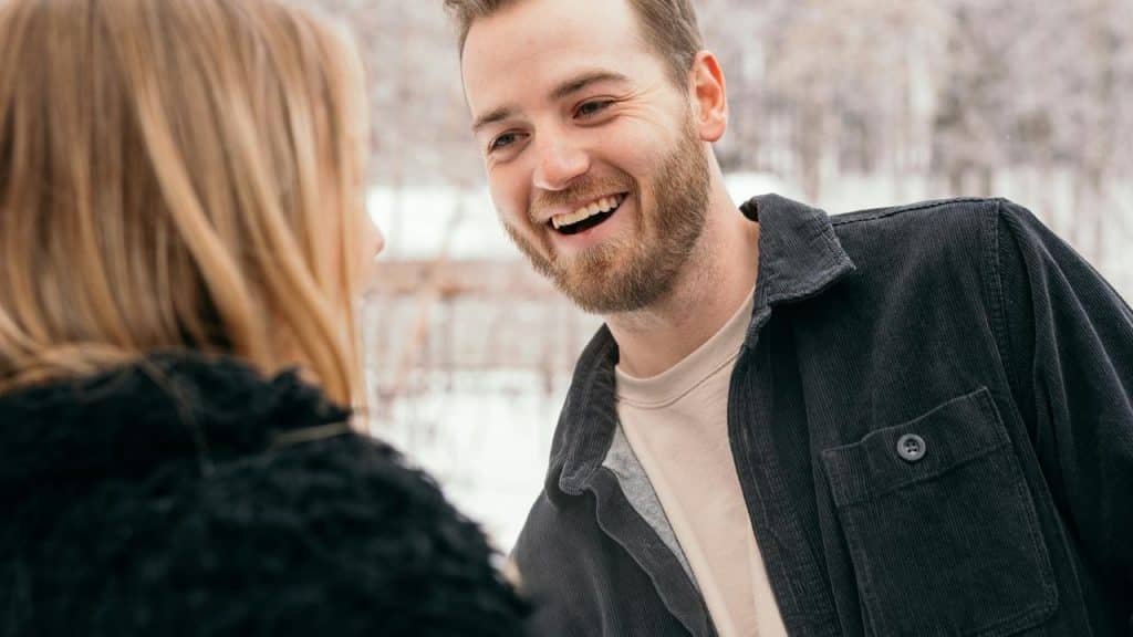 A smiling man talks with a woman outdoors.