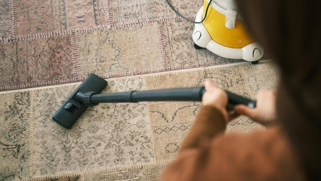 A person vacuums a patterned rug with a yellow vacuum cleaner.