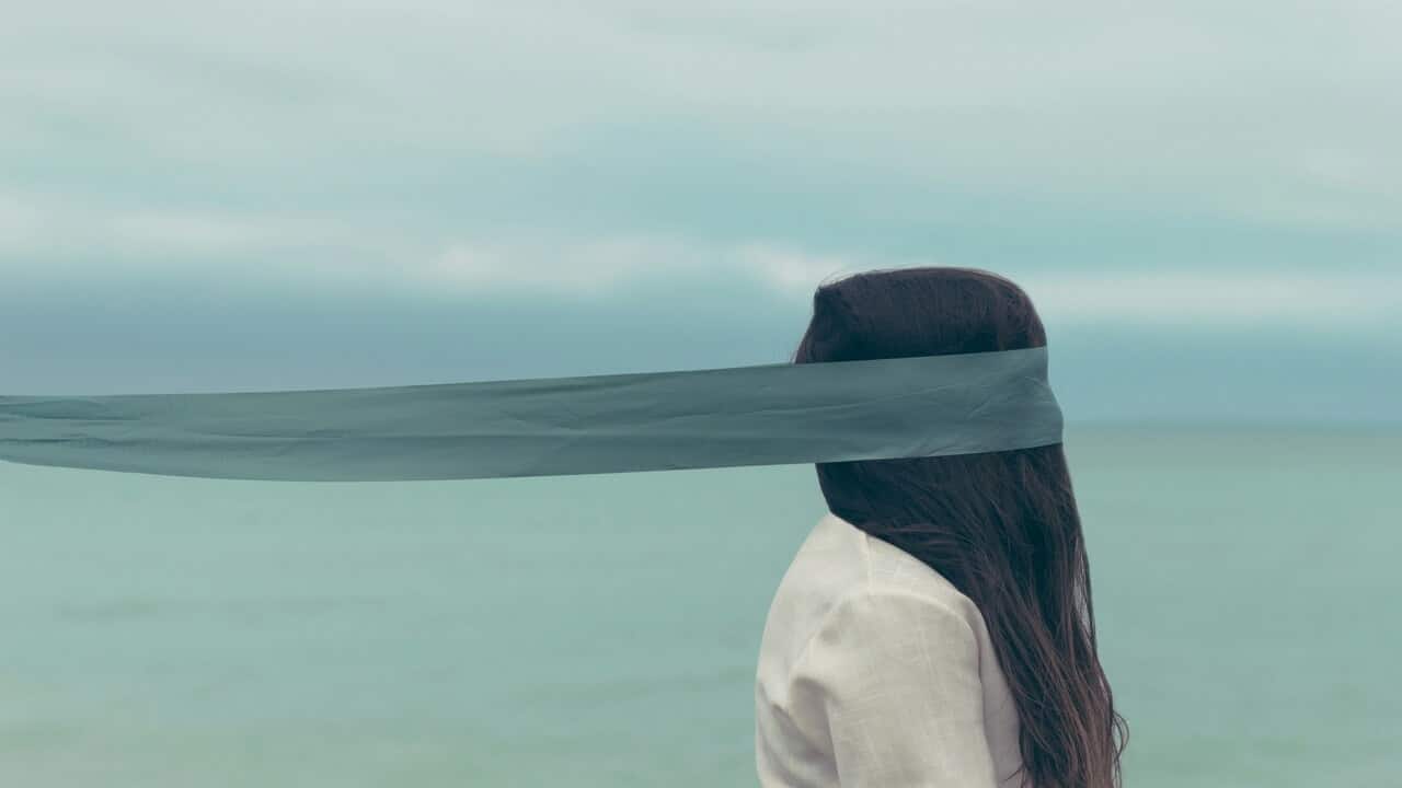 A woman’s face being covered by a black blindfold