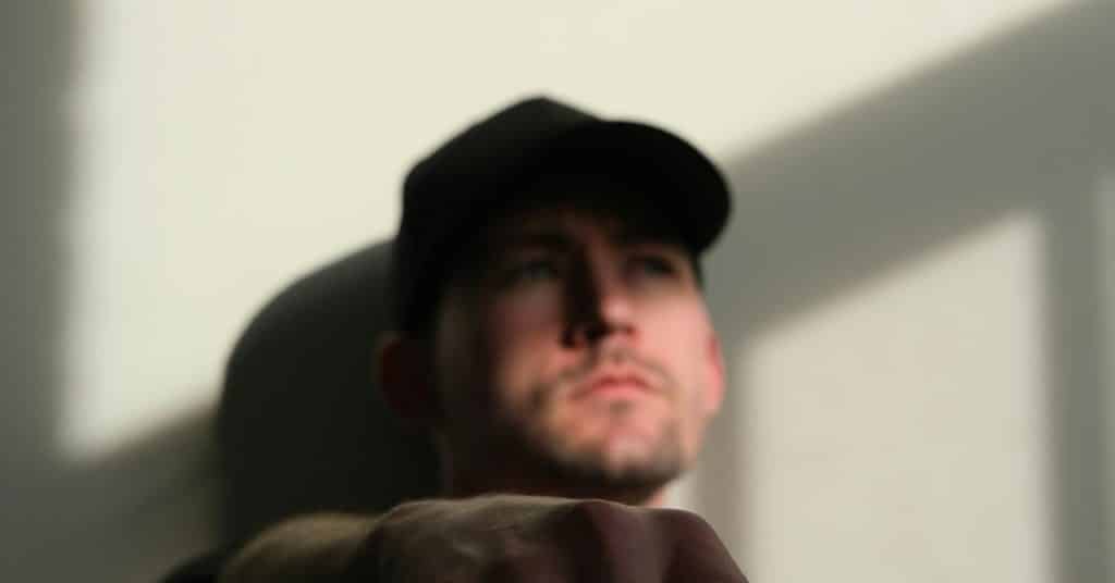 A man wearing a cap, gazing ahead in soft, directional light indoors.