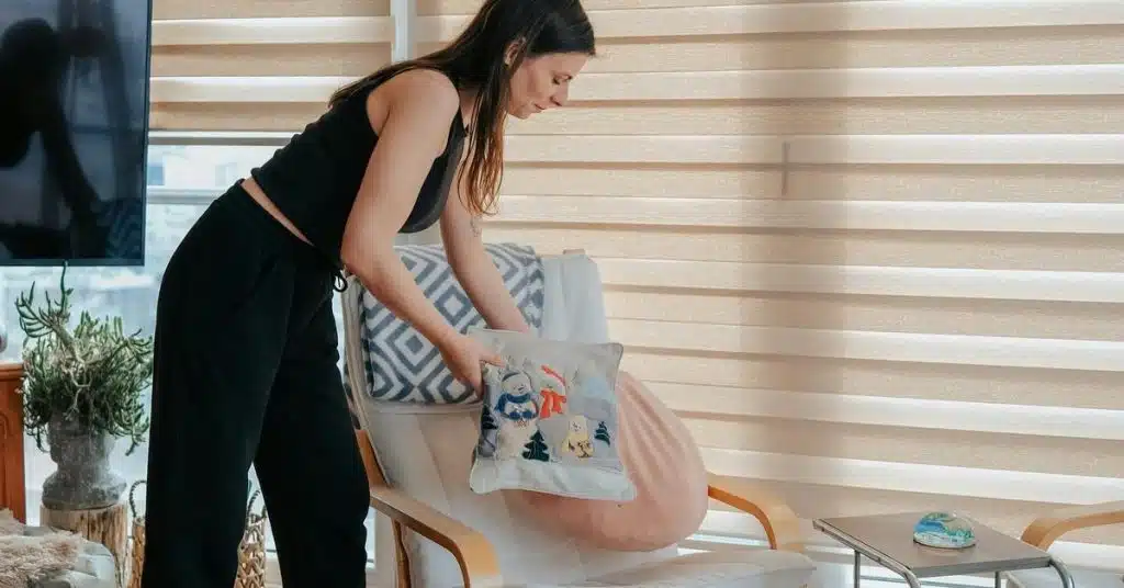 A woman adjusting a decorative pillow on a chair in a bright living room.