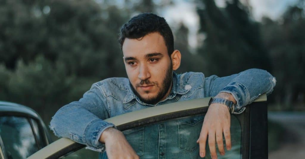 A man leaning on a car door outdoors, looking thoughtful.