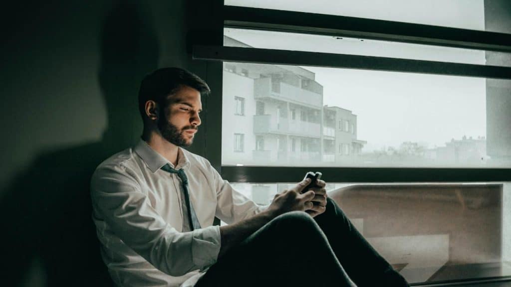A man sitting by a window looking at his phone.