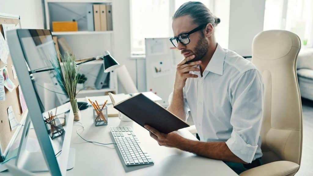 A man in an office reading a notebook at his desk.