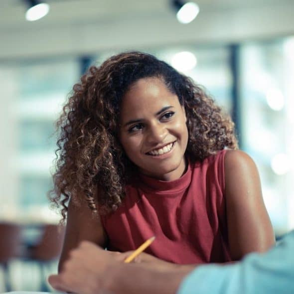 A smiling woman talks with a colleague across a table in an office.