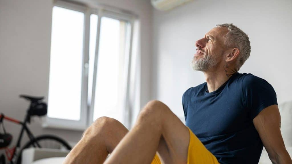 An older man sitting indoors and gazing upward.