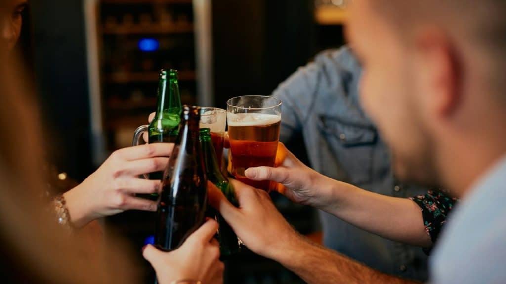 A group of people clinking beer bottles and glasses together.