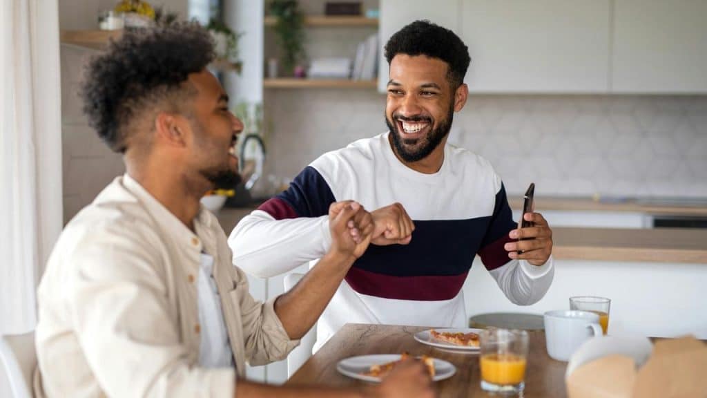 A man smiling and bumping fists with another man while eating at a table.