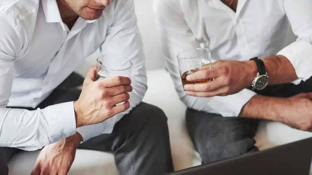 A close-up of two men in white shirts holding glasses of whiskey.