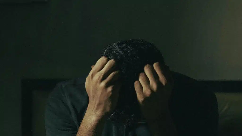 A person sits with their head down, holding their hair in distress.