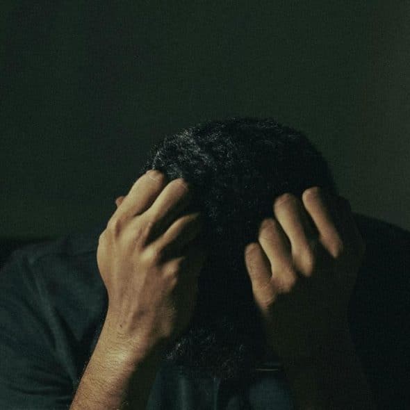A person sits with their head down, holding their hair in distress.
