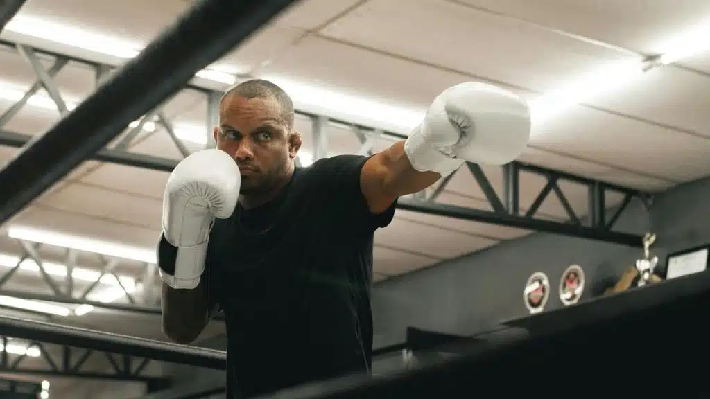 A man wearing white boxing gloves practicing in a gym ring.