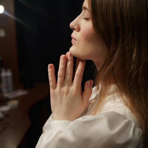 A woman with closed eyes holds her hands together in a quiet moment.