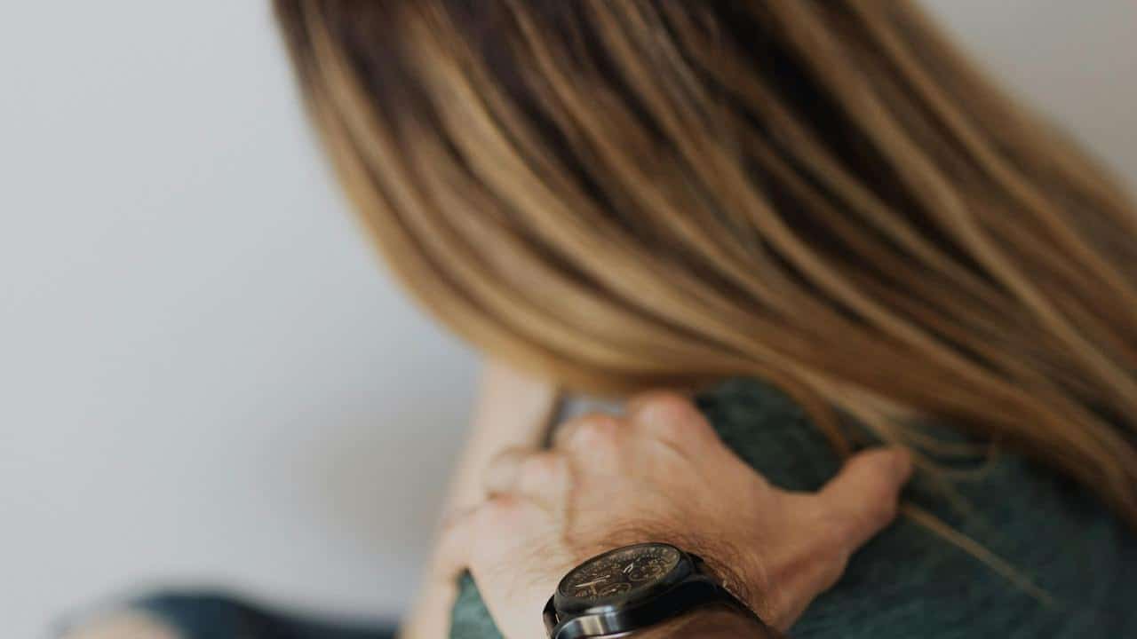 A person rests a comforting hand on a woman’s shoulder.