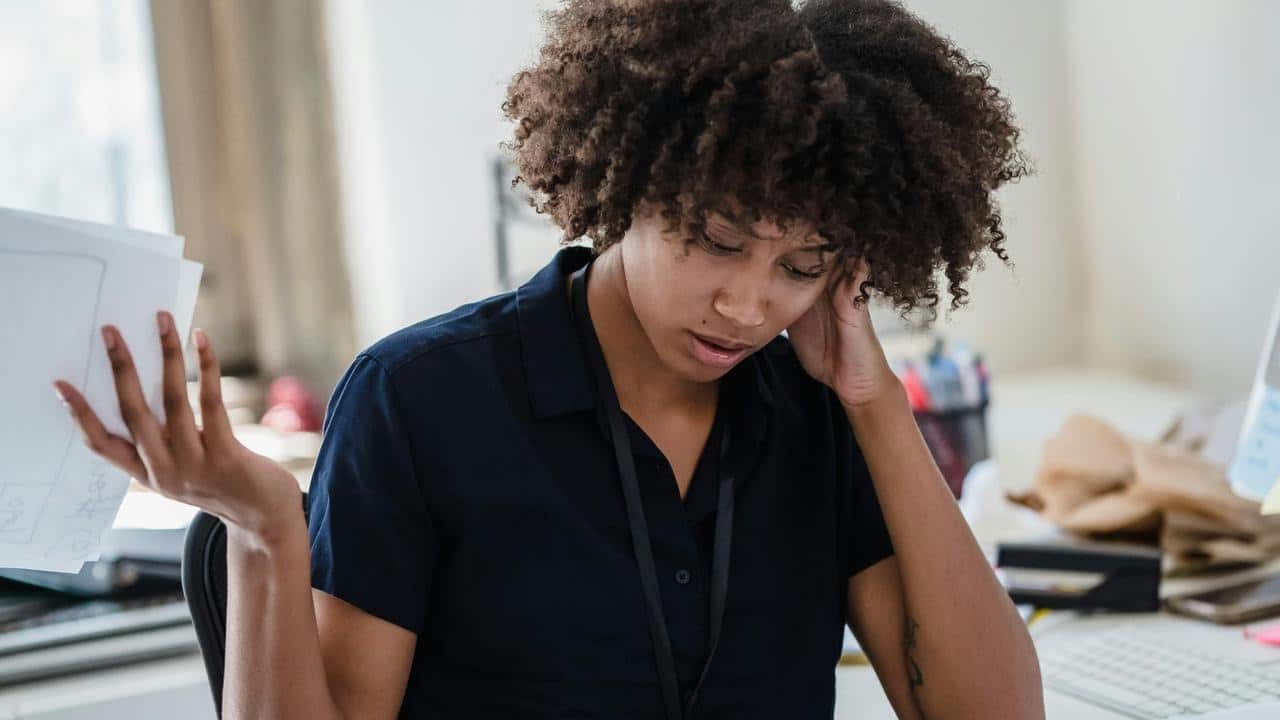 A woman at a desk looks stressed while holding papers.