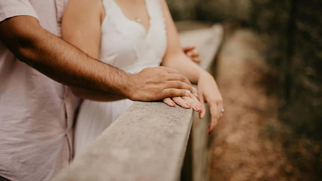 A couple stands close together with their hands resting on a railing.