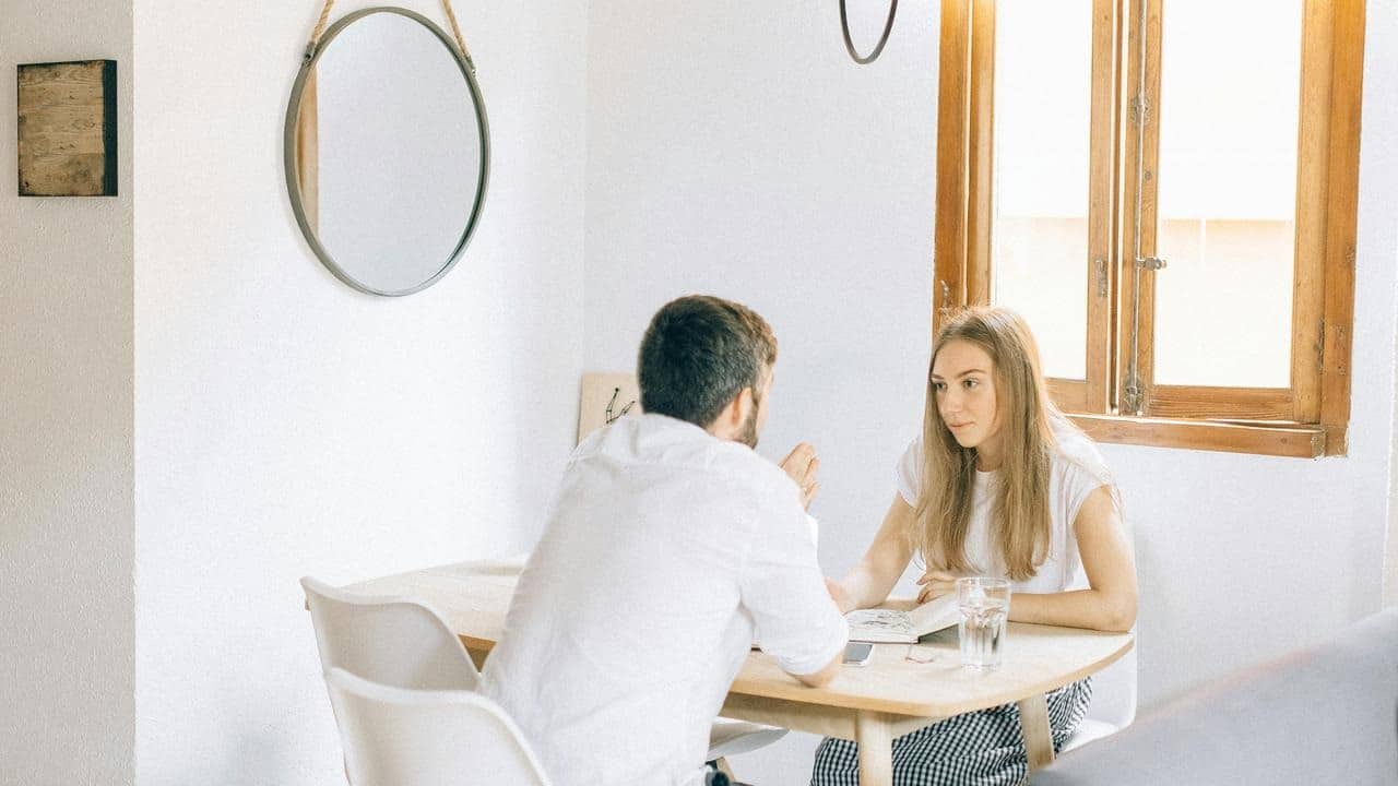 A man and woman sit at a small table having a conversation.
