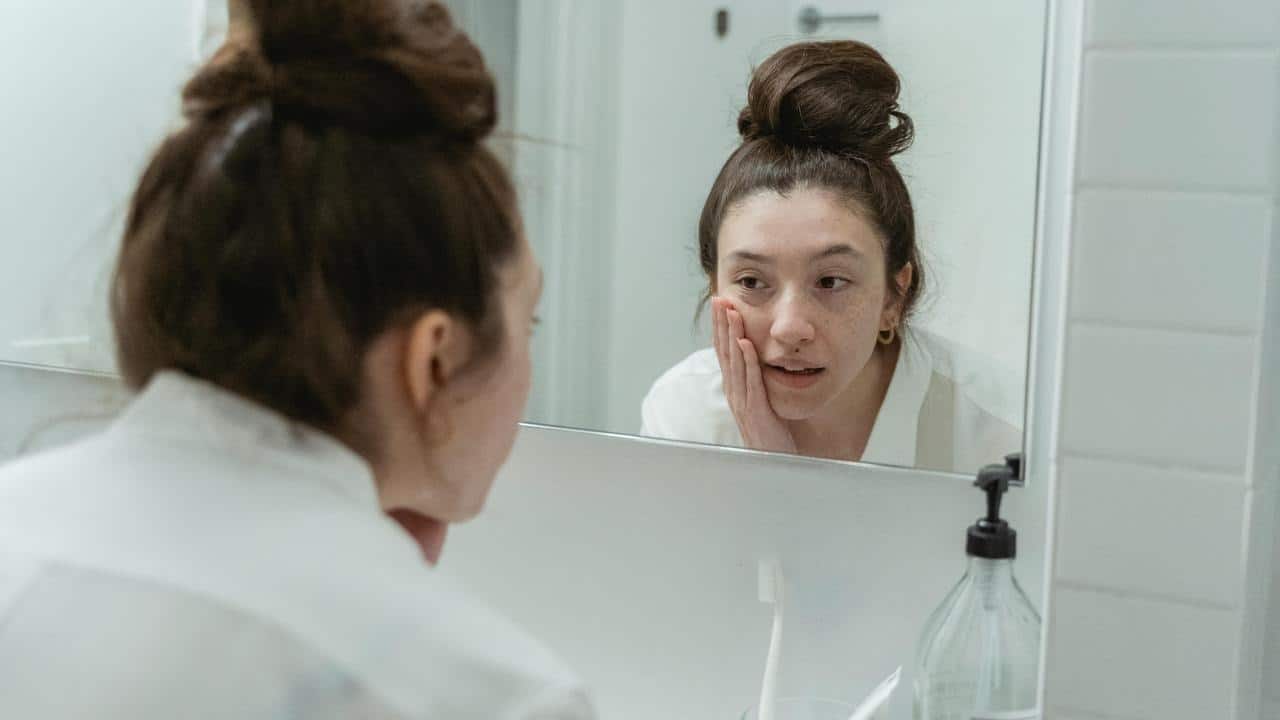 A young woman looks at herself in a bathroom mirror.