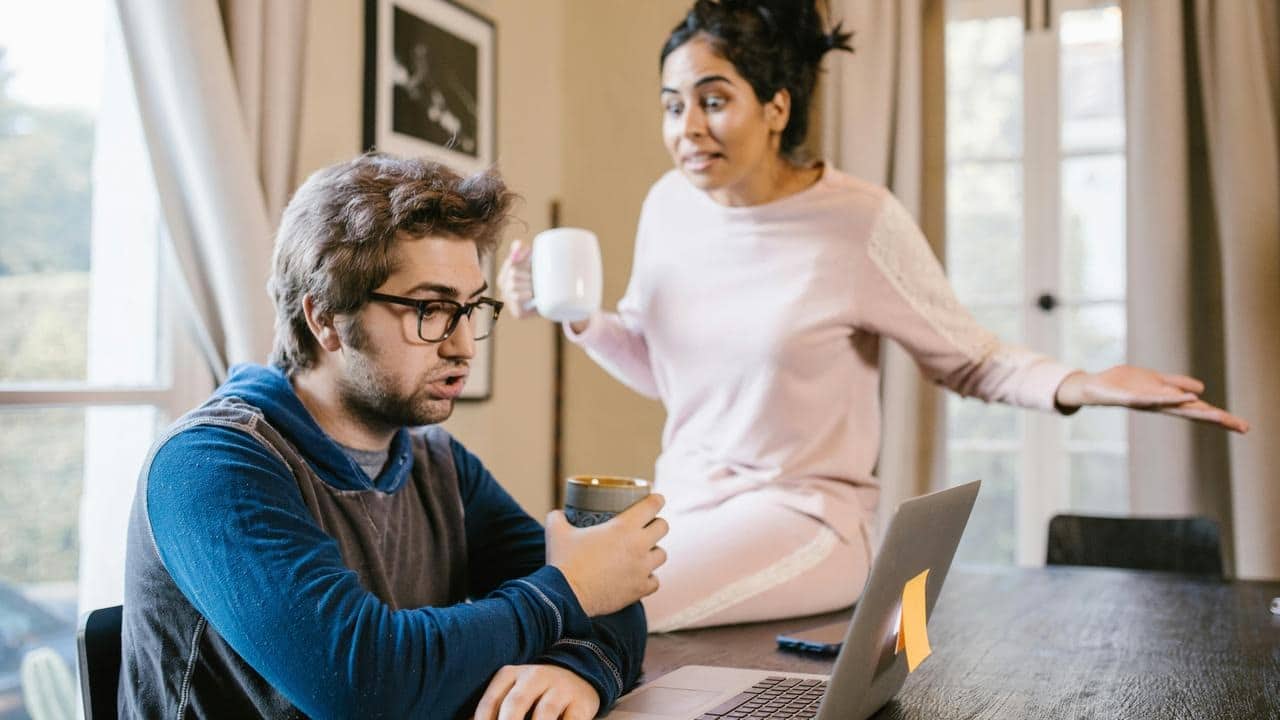 A woman gesturing in frustration while a man focuses on his laptop.