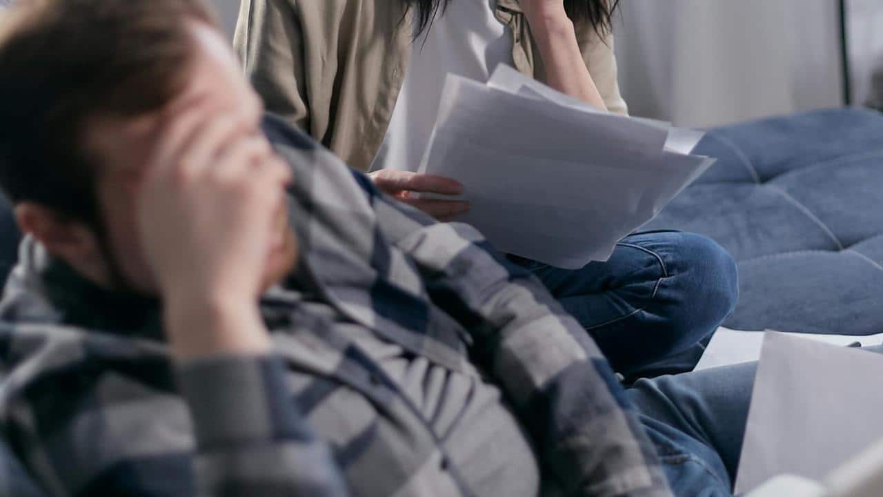 A couple sitting with bills, both appearing stressed and overwhelmed.