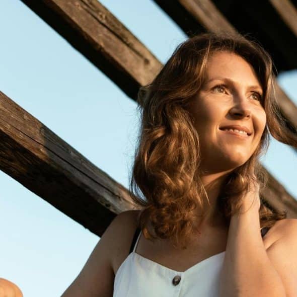 A woman smiles while standing outdoors near wooden beams.