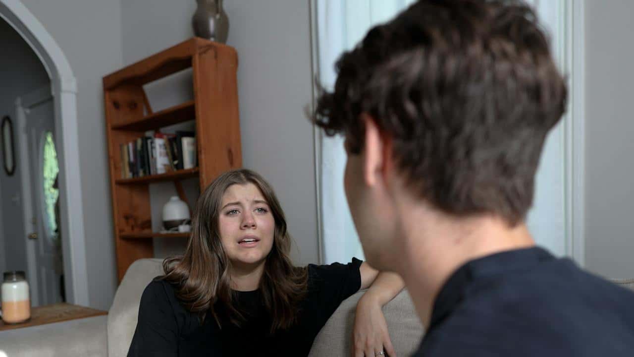 A woman complaining to her husband while sitting at a couch indoors.