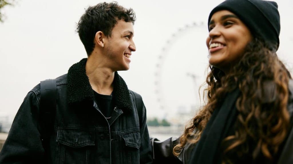 A smiling couple talking outdoors, with a Ferris wheel in the background.