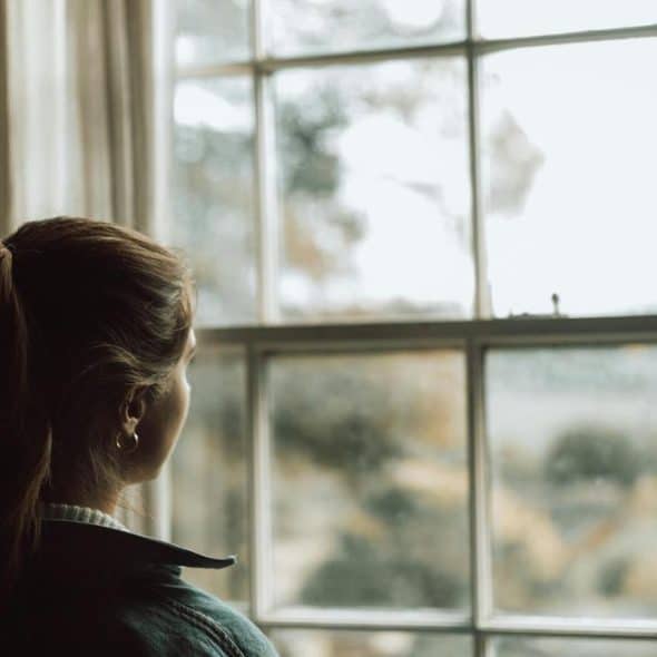 A woman with a ponytail looks out a large window on a cloudy day.