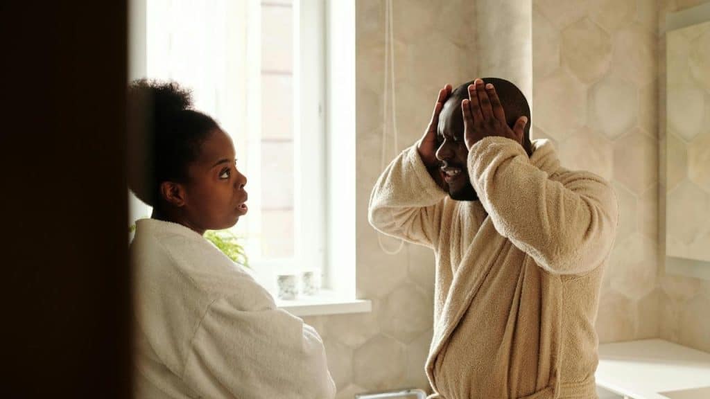 A man and woman in bathrobes having a serious conversation in a bathroom.