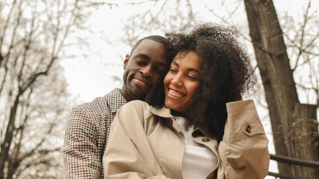 A couple smiling and embracing outdoors among trees.