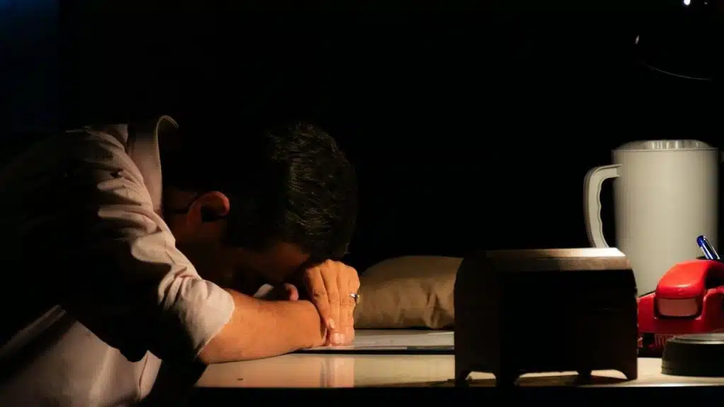 A close-up of a tired man with his head down on a desk.