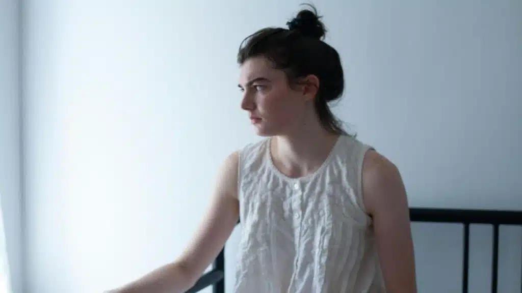 A woman sitting alone in a bedroom.