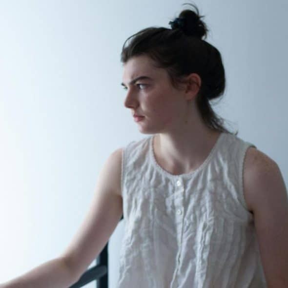 A woman sitting alone in a bedroom.
