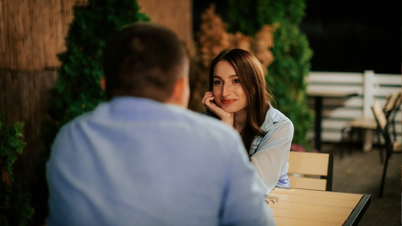 A romantic woman looking in the eyes of a man sitting with her at a table in a restaurant.
